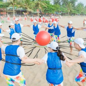 Đội chơi trò giữ bóng lớn bằng dây đai ngoài bãi biển – Minh họa rõ nét cho _Đồng tâm hiệp lực_ hoặc các trò phối hợp nhịp nhàng