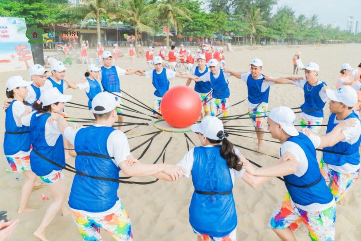 Đội chơi trò giữ bóng lớn bằng dây đai ngoài bãi biển – Minh họa rõ nét cho _Đồng tâm hiệp lực_ hoặc các trò phối hợp nhịp nhàng